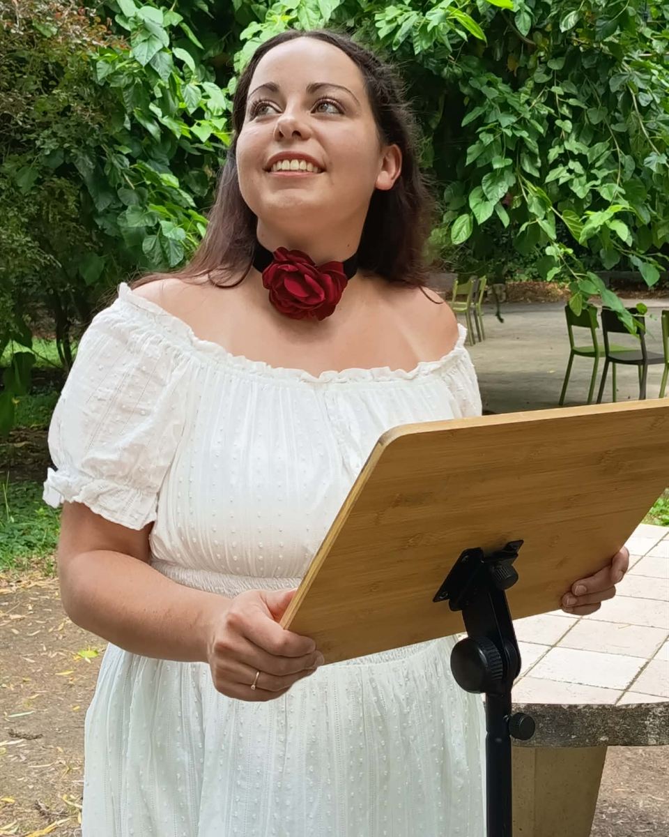 Marjorie, prêtresse païenne, souriante au pupitre lors d'une célébration en plein air, rose rouge au cou